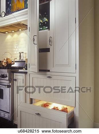 Stock Photography - KITCHENS - Pantry on top of SUB-ZERO 700 series base freezer. Narrow pullouts on either side of range, white and stainless steel, raised panel cabinet doors, subway tile, copper tea kettle,. Fotosearch
