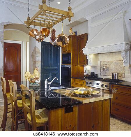 KITCHENS - Upscale country/traditional look, overall of island and stove. Custom wood cabinets with warm stain. Copper pots hang from rack. Bar stools, straight edge granite counters, inset wood cutting board, molding, range hood with plaster corbels, and View Large Photo Image Stock Photograph - KITCHENS - Upscale country/traditional look, overall of island and stove. Custom wood cabinets with warm stain. Copper pots hang from rack. Bar stools, straight edge granite counters, inset wood cutting board, molding, range hood with plaster corbels, and. Fotosearch