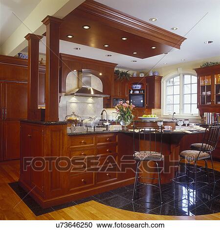 KITCHENS - View of cherry and granite island with lots of curves, eating area, wood and tile flooring, decoration columns. Exhaust hood in background, iron stools, recessed lighting, ceramic flying pig, arched window, molding, tulips View Large Photo Image Stock Image - KITCHENS - View of cherry and granite island with lots of curves, eating area, wood and tile flooring, decoration columns. Exhaust hood in background, iron stools, recessed lighting, ceramic flying pig, arched window, molding, tulips. Fotosearch
