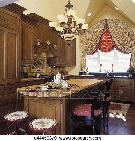 KITCHENS view of island, stove and sink area, fabric window treatments, white wooden shutters over sink. Medium dark wood cabinets, French country style, arched window and treatment, roosters painted on top of stools, chandelier, coffee set up View Large Photo Image Stock Image - KITCHENS view of island, stove and sink area, fabric window treatments, white wooden shutters over sink. Medium dark wood cabinets, French country style, arched window and treatment, roosters painted on top of stools, chandelier, coffee set up. Fotosearch
