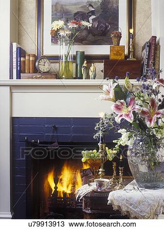 LIVING ROOMS - Detail of fireplace, foreground crystal vase with stargazer lilies, brass candlesticks, mantel display of books, Asian sculptures, clock, wooden boxes, vase of flowers View Large Photo Image Stock Image - LIVING ROOMS - Detail of fireplace, foreground crystal vase with stargazer lilies, brass candlesticks, mantel display of books, Asian sculptures, clock, wooden boxes, vase of flowers. Fotosearch