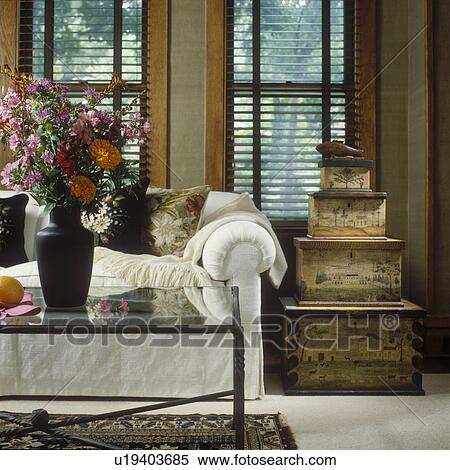 LIVING ROOMS - Eclectic Living Room. Detail of wooden painted boxes sitting on floor next to sofa, windows with wood blinds, white slip covered sofa, glass and iron coffee table, vase of flowers. View Large Photo Image Stock Photography - LIVING ROOMS - Eclectic Living Room. Detail of wooden painted boxes sitting on floor next to sofa, windows with wood blinds, white slip covered sofa, glass and iron coffee table, vase of flowers. . Fotosearch