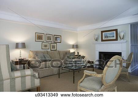 Stock Photo - LIVING ROOMS: traditional soft colors, fireplace with white mantel, Louis style chairs, glass top table, antique scale, sisal rug, framed art over sofa, striped wingchair to left. Fotosearch