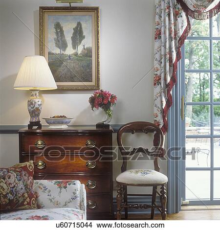 Picture - LIVING ROOMS - Traditional, vignette of chest of drawers & ballon back Victorian chair, French door with scarf floral drape with dark fringe, section of floral sofa shows in left corner, painting above chest. . Fotosearch