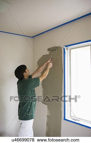 Stock Photo - Man painting wall with roller by the window. Fotosearch