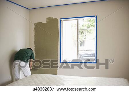 Stock Photo - Man painting wall with roller in the bedroom. Fotosearch
