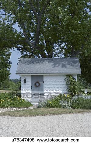 OUTBUILDINGS: farm garden shed, small white painted concrete block building with grey roof and door, wreath on door, stone path, daylily and lambs ear, trellis with vines View Large Photo Image Stock Photo - OUTBUILDINGS: farm garden shed, small white painted concrete block building with grey roof and door, wreath on door, stone path, daylily and lambs ear, trellis with vines. Fotosearch