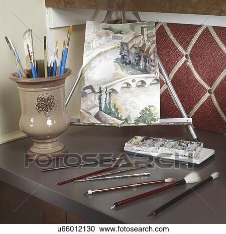 Stock Image - Painting on easel with art products at counter. Fotosearch