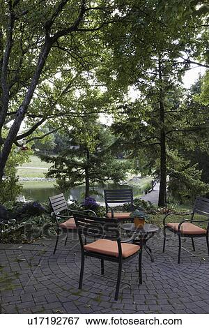 Stock Photo - PATIO: circular brick design patio, four chairs with orange cushions, lake view, shaded. Fotosearch