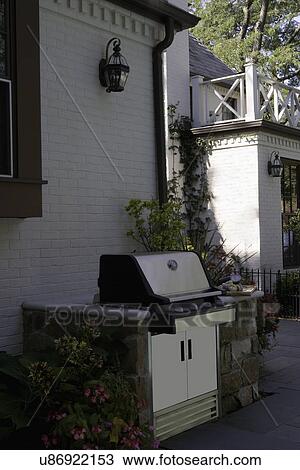 Stock Image - PATIO; close up of barbeque, white brick house. Fotosearch