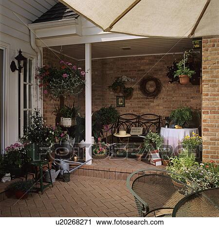 Stock Image - PATIOS: Brick patio and home, container gardens, covered porch with bench and potted flowers. Fotosearch