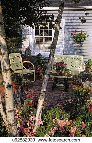 Patios: Brick patio surrounded by a free form flower garden. Grey frame cottage in background, vintage pale yellow metal lawn chairs, birch tree. View Large Photo Image Stock Image - Patios: Brick patio surrounded by a free form flower garden. Grey frame cottage in background, vintage pale yellow metal lawn chairs, birch tree.. Fotosearch
