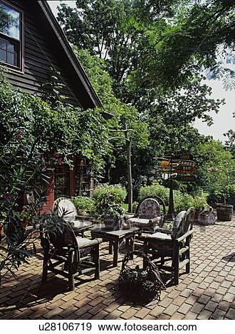 Stock Photo - Patios: Brick patio with twig table and chairs with cushions, off living room, frame house with French doors, trellis on house covered in vines. . Fotosearch