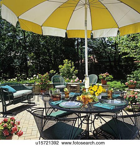 PATIOS: Close up of umbrella table and surrounding wicker furniture, small stone wall defines patio area. Yellow and white umbrella. View Large Photo Image Stock Image - PATIOS: Close up of umbrella table and surrounding wicker furniture, small stone wall defines patio area. Yellow and white umbrella.. Fotosearch