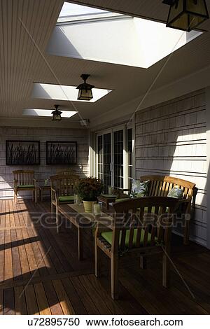 Stock Image - PATIOS: covered porch/ deck area, skylights in roof, Arts and Crafts outdoor lighting, cedar shake, teak furniture with lime green cushions, metal cattail sculptures on wall. Fotosearch