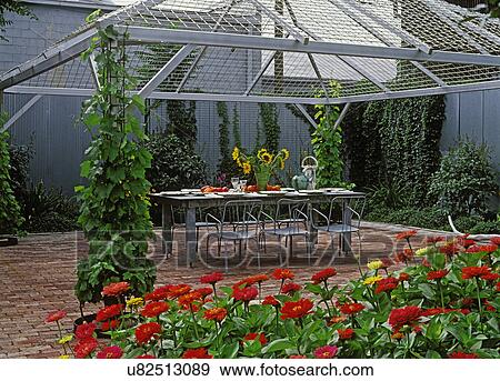 Patios: Eating area, large metal table set for dinner party, brick floor, mesh metal pavilion over eating area, red zinnias in foreground. Metal privacy fence. View Large Photo Image Stock Photo - Patios: Eating area, large metal table set for dinner party, brick floor, mesh metal pavilion over eating area, red zinnias in foreground. Metal privacy fence.. Fotosearch
