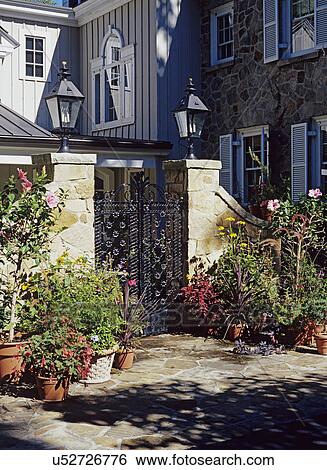 Stock Photograph - PATIOS: Flagstone walled patio with container garden in front of entrance with iron gates. Hibiscus, Purple Fountain Grass, Rubekia, coleus, Gardenmeister fuschia.. Fotosearch