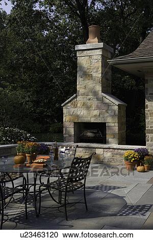 Stock Image - PATIOS: outdoor fireplace with dining table in foreground, fall flowers, pumpkins, wine glasses. Fotosearch