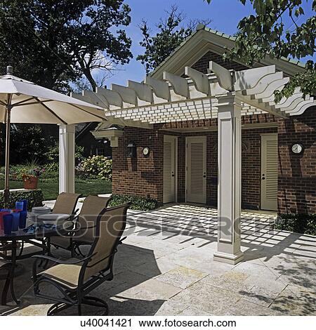 Stock Image - PATIOS: Patio eating area off red brick pool house with white wood portico. Iowa limestone, umbrella glass top table with chairs, lawn off to the left.. Fotosearch