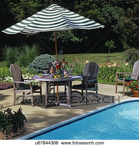 PATIOS: Pool side patio, with flower border garden. Table with striped umbrella and chairs. Purple cone flowers, ornamental grass, pansies. View Large Photo Image Stock Photograph - PATIOS: Pool side patio, with flower border garden. Table with striped umbrella and chairs. Purple cone flowers, ornamental grass, pansies. . Fotosearch