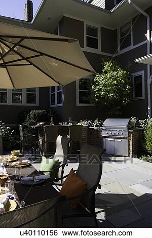 PATIOS: Umbrella to left with rectangular dining table, off to right is a built in gas grill and bar area with wicker barstools View Large Photo Image Stock Photograph - PATIOS: Umbrella to left with rectangular dining table, off to right is a built in gas grill and bar area with wicker barstools. Fotosearch