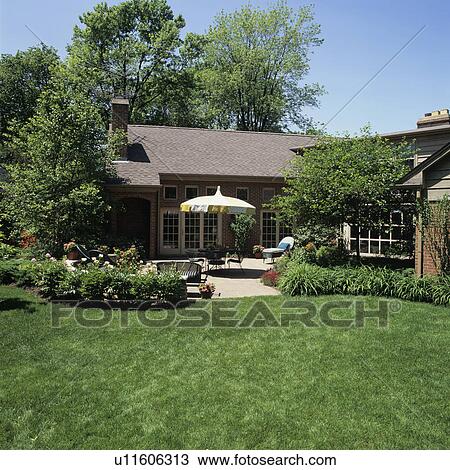 PATIOS: View from lawn towards patio area with a yellow and white umbrella over table, patio furniture, brick floor, peony bushes. Brick home, French doors. View Large Photo Image Stock Image - PATIOS: View from lawn towards patio area with a yellow and white umbrella over table, patio furniture, brick floor, peony bushes. Brick home, French doors.. Fotosearch
