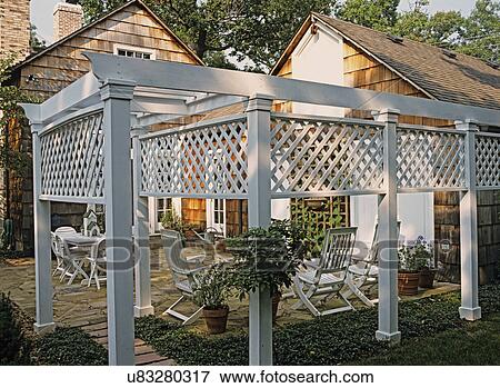 Stock Photo - Patios: View inside patio area looking out. White trellis privacy divide. Flagstone patio area with white chairs and table.. Fotosearch