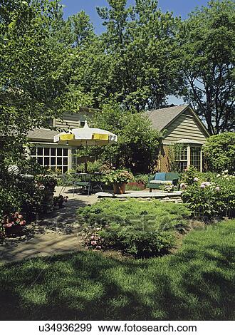 Stock Photo - PATIOS: View towards house with patio area, umbrella table, and green patio furniture, a low small stone wall circles along the edge of the patio area, brick home. . Fotosearch