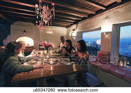 Stock Image - People sharing a meal at wooden dining table, Mykonos, Greece. Fotosearch