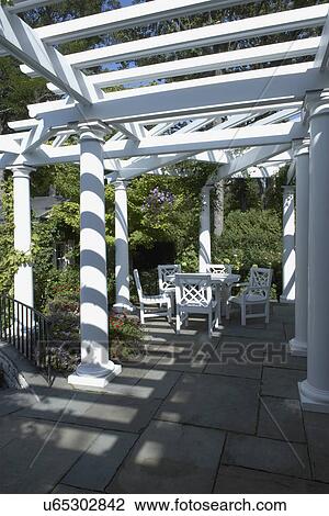 PERGOLAS: Classical white columned pergola, grey slate patio, Chinese Chippendale style patio set, angle view, black iron railing curves to left View Large Photo Image Stock Image - PERGOLAS: Classical white columned pergola, grey slate patio, Chinese Chippendale style patio set, angle view, black iron railing curves to left. Fotosearch