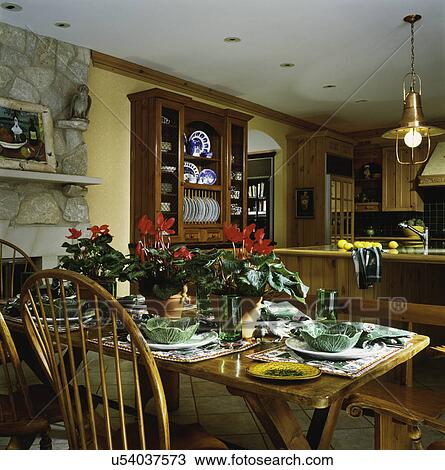 Stock Image - Pine hutch, limestone fireplace, dining area with place settings on dining table, blooming cyclamen. Fotosearch