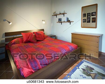 Stock Image - Platform bed with red comforter; Italy. Fotosearch