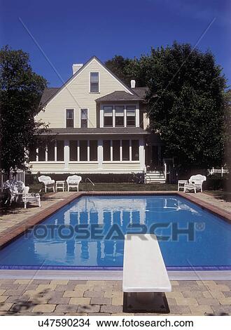POOLS: Backyard pool, rectangle shape, remodeled/restored Victorian frame house in backyard, brick and stone surround pool, diving board, white wicker furniture View Large Photo Image Picture - POOLS: Backyard pool, rectangle shape, remodeled/restored Victorian frame house in backyard, brick and stone surround pool, diving board, white wicker furniture. Fotosearch