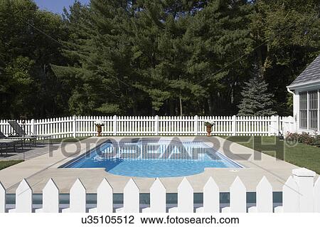 Stock Image - Pools: view taken from picket fence across length of pool. Area surrounded by white picket fence, part of house visible on right. Trees in background. Fotosearch