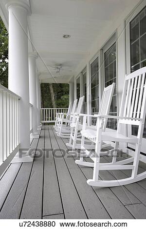 Stock Image - PORCH: all white porch, classic columns with four white rocking chairs, row of windows, composite deck materials. Fotosearch