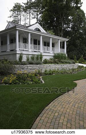 PORCH: Classic columned porch on a small cottage, garden retaining wall, perennial beds lawn and a brick curving walkway View Large Photo Image Stock Photography - PORCH: Classic columned porch on a small cottage, garden retaining wall, perennial beds lawn and a brick curving walkway. Fotosearch