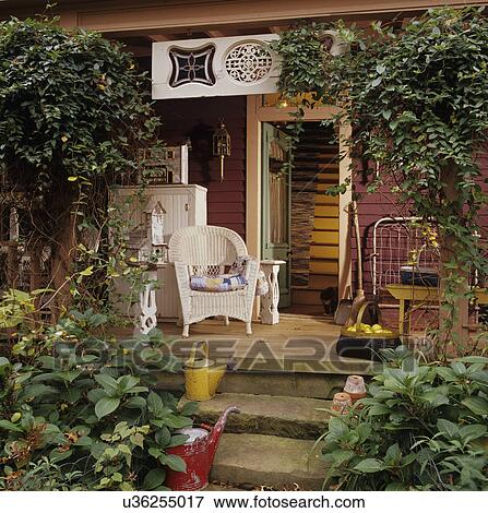 PORCH: Country porch, open door, wicker chair, watering cans on concrete steps, folk art and architectural salvage decorate, climbing vines, autumn season View Large Photo Image Stock Photo - PORCH: Country porch, open door, wicker chair, watering cans on concrete steps, folk art and architectural salvage decorate, climbing vines, autumn season. Fotosearch