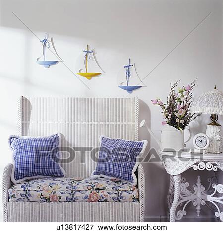 Stock Photo - PORCH: DETAIL white wicker settee, Victorian wicker table, three sailboats on wall, plaid pillows, watering can filled with flowers. Fotosearch