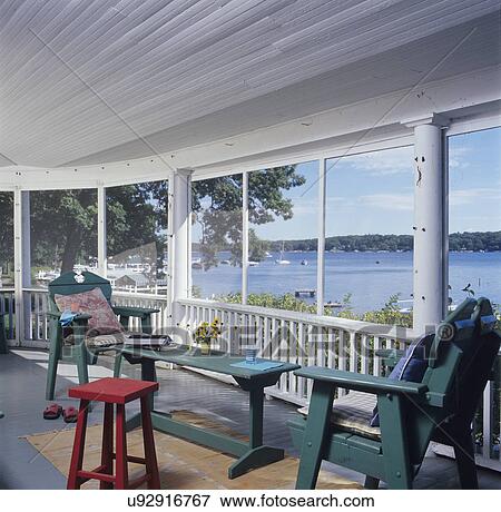 PORCH: Scenic lake view from a large curved screen porch of a summer lake home from the 1920's. casual with green chairs and red stool. View Large Photo Image Stock Photo - PORCH: Scenic lake view from a large curved screen porch of a summer lake home from the 1920's. casual with green chairs and red stool.. Fotosearch