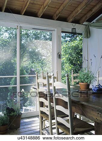 Stock Photograph - PORCH: Screened porch, casual country, rustic pine farm table, ladder back chairs with rush seats, potted lavender on table, simple. Fotosearch