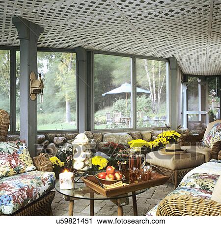 Stock Image - PORCH: underneath deck, a screened porch, lattice ceiling, mums, glass table with tray of cider, vase of white pumpkins. Fotosearch