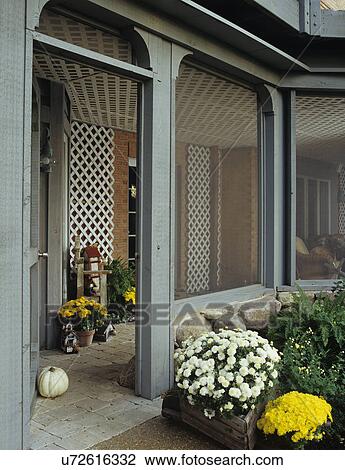 Stock Image - PORCH: Underneath deck, screened porch, fall season, doorway, stone pavers, white mum to right of door. Fotosearch