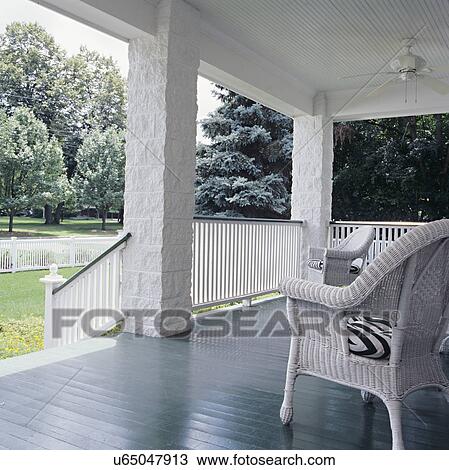 Stock Image - PORCH: White wainscot ceiling with fan, dark green painted floors, white wicker on front porch of a four square farmhouse in the suburbs, two wicker chairs no plants simple. Fotosearch