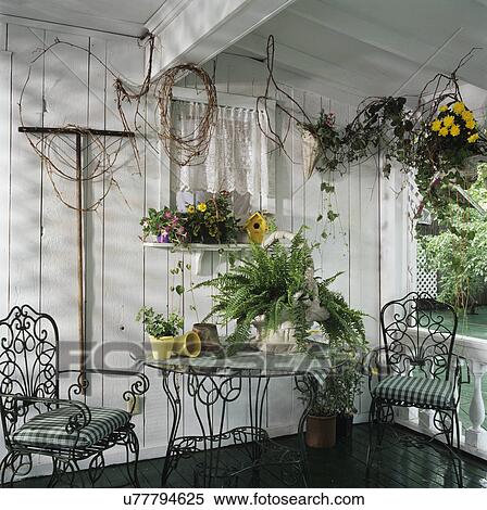 Stock Photography - PORCHES: Green and white, corner area, iron chairs and table, wall decorated with grapevine, Boston fern, shelf with potted flowers and birdhouse. Fotosearch