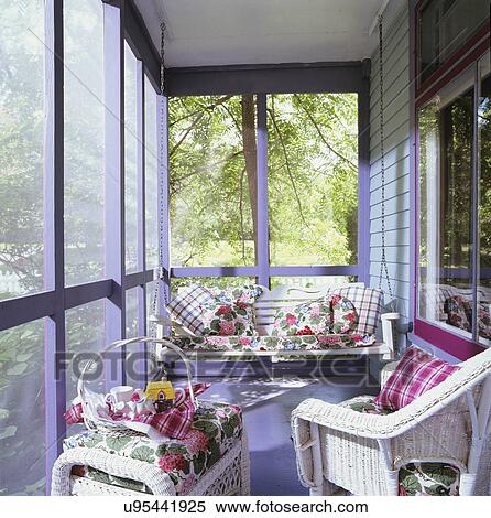Stock Photography - PORCHES: Screened porch, colorful wood frame house, periwinkle blue and fuschia painted trim, swing, white wicker chairs, vintage floral fabrics used to cover pillows . Fotosearch