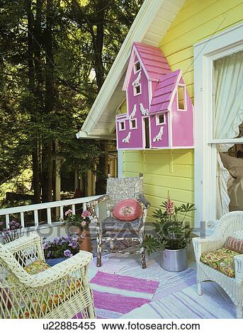 Stock Photography - PORCHES: Second story porch on vacation home. Yellow frame house, elaborate hot pink birdhouse on exterior wall, white wicker furniture, cottage style, area rugs, flowers . Fotosearch