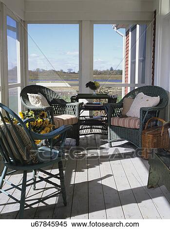 Stock Photography - PORCHES: STRAIGHT shot toward two green wicker chairs with striped cushions, wicker tea table, Windsor chair to left, screen ed porch, sunflowers, view to lake. Fotosearch