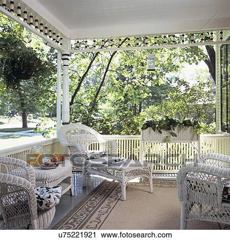 Stock Image - PORCHES: Victorian covered porch with fretwork, white wicker, area rug, cottage style, . Fotosearch