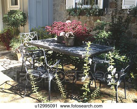 Stock Image - Potted plants on table with chairs in backyard. Fotosearch