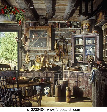 RUSTIC HOMES AND CABINS - Interior shot of Primitive rustic kitchen, with old corner cupboard with old pottery and cooking utensils etc, log and chink walls, distressed cabinets, sponge ware, wooden bowls and utensils, butter churns, old tins View Large Photo Image Picture - RUSTIC HOMES AND CABINS - Interior shot of Primitive rustic kitchen, with old corner cupboard with old pottery and cooking utensils etc, log and chink walls, distressed cabinets, sponge ware, wooden bowls and utensils, butter churns, old tins. Fotosearch